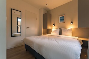 A bedroom with a bed, bedside lamps, a mirror, and a painting on the wall.