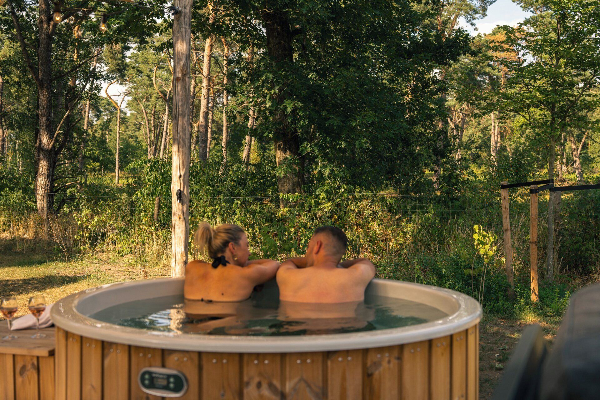 A hot tub in a wooded area with a wooden fence and trees in the background.