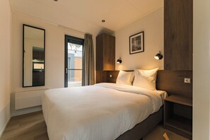 Une chambre d’hôtel avec un grand lit, un miroir, une fenêtre avec des rideaux, un tableau accroché au mur et une table de chevet.
