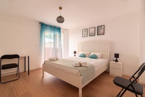 A bedroom with a bed, a chair, a small table, a nightstand, and a lamp.