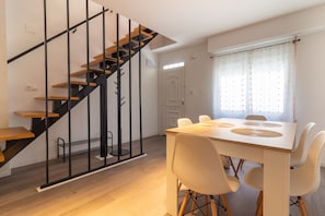 A modern interior with a staircase, dining table, chairs, and a window with curtains.