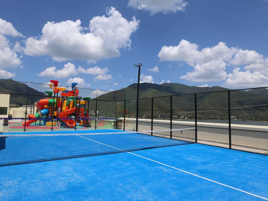 Un parque infantil con toboganes y estructuras para escalar, una cancha deportiva azul y una vista de la montaña al fondo.