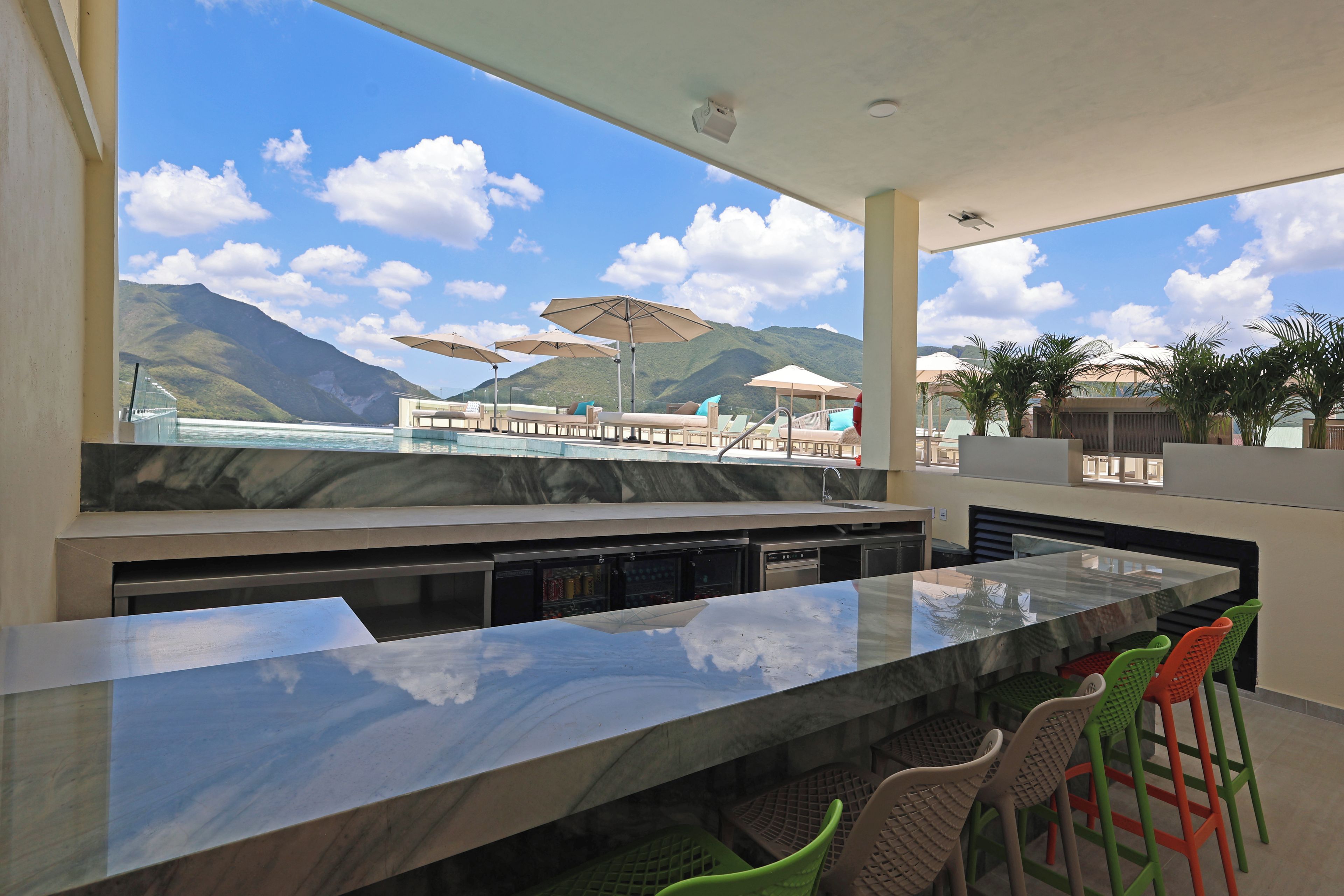 A modern outdoor bar area with a view of mountains and a pool.