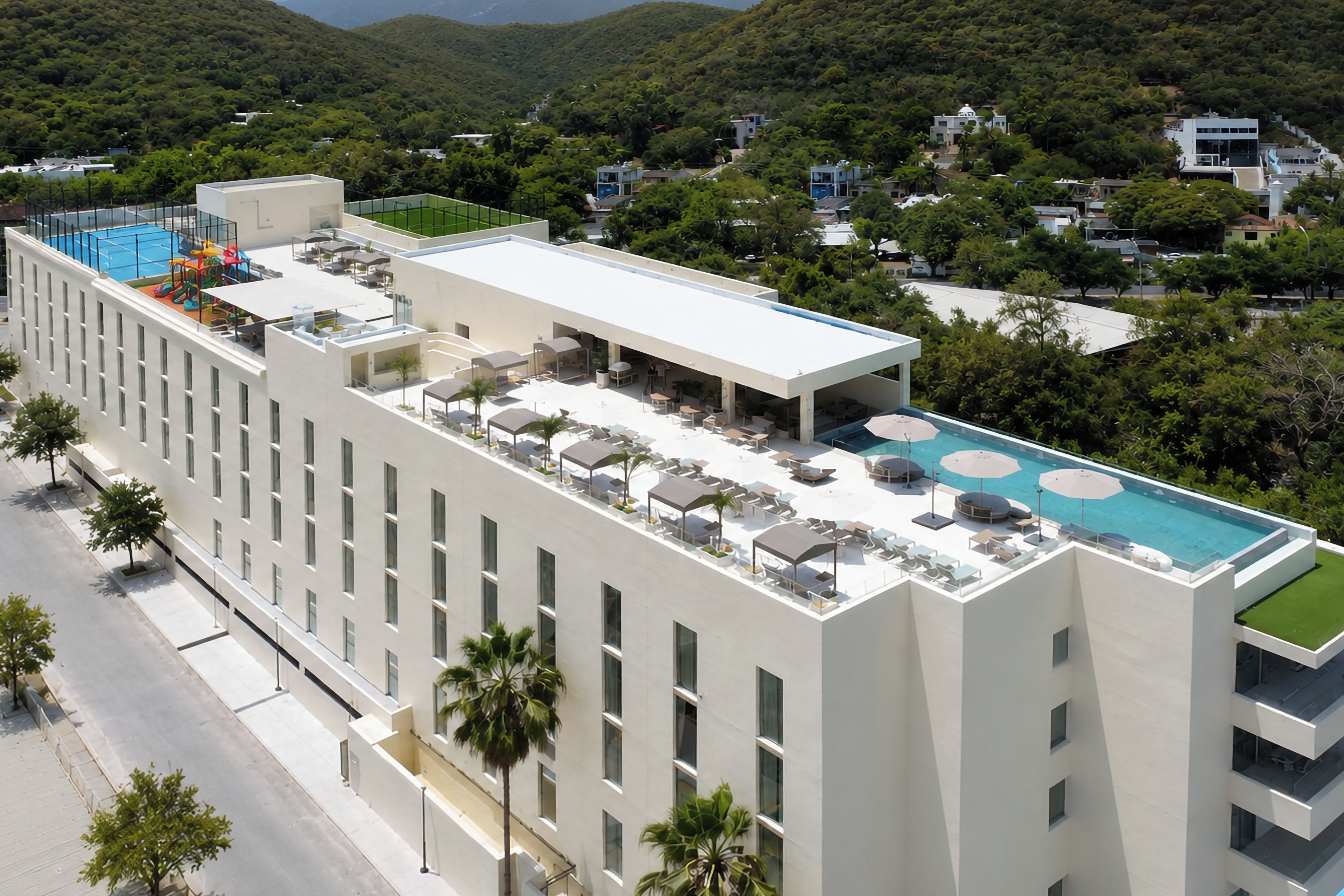 A modern hotel with a rooftop pool, multiple dining areas, and a view of surrounding greenery.