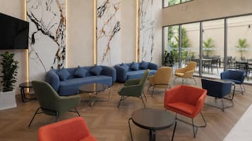 A modern lounge area with a blue sofa set, green and red chairs, and a wooden floor.