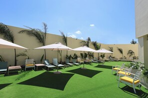 A sunlit outdoor seating area with multiple lounge chairs and umbrellas, surrounded by greenery and a low wall. - Holiday Inn Resort Monterrey Santiago by IHG (Santiago)