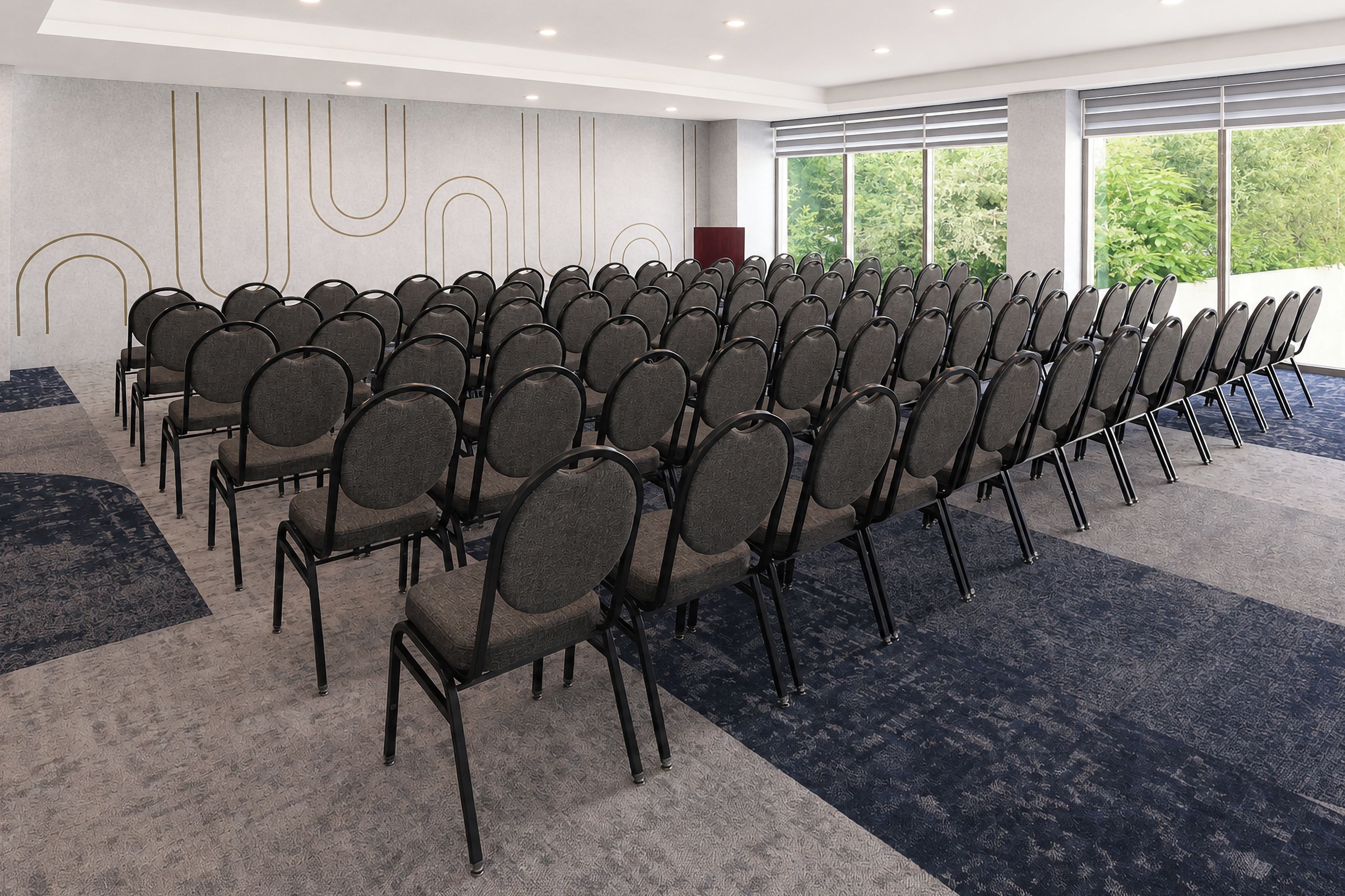 Une salle de conférence avec des rangées de chaises, un pupitre et de grandes fenêtres.