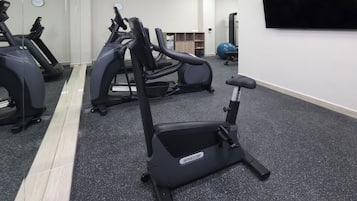 Een sportschool met hometrainers, een loopband en een elliptische machine.