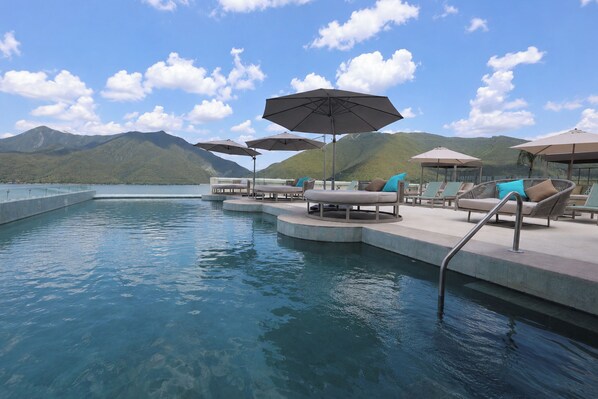 A pool area with lounge chairs and umbrellas, surrounded by mountains.
