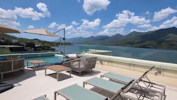 A poolside area with lounge chairs and a table, overlooking a lake with mountains in the background.