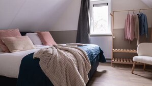 Ein Schlafzimmer mit Bett, Fenster, Heizkörper, Sessel und Kleiderstange.
