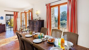 A dining area with a wooden table set for breakfast, wicker chairs, and a view through a glass door. - Moulin St Jean - Nature in the heart of the village (Tourrettes-sur-Loup)