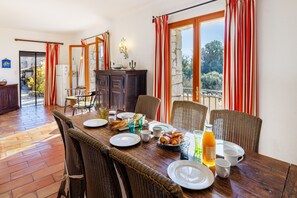 Ein Essbereich mit einem Holztisch, gedeckt für ein Frühstück, Weidekörbchenstühlen und Blick durch eine Glastür.