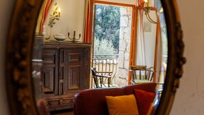 A round mirror reflecting a room with a wooden cabinet, a red sofa, and a window with curtains. - Moulin St Jean - Nature in the heart of the village (Tourrettes-sur-Loup)