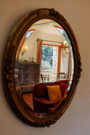 Ein runder Spiegel, der einen Raum mit einem Holzschrank, einem roten Sofa und einem mit Vorhängen drapierten Fenster zeigt.