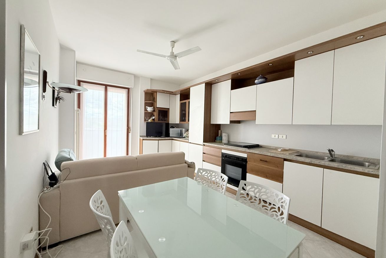 A modern kitchen with white cabinets, a dining area with a glass table, and a ceiling fan.