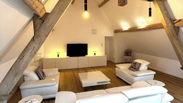 A loft-style living room with exposed wooden beams, a flat-screen TV, white sofas, and a coffee table. - Château de Foussal (Plaisance)