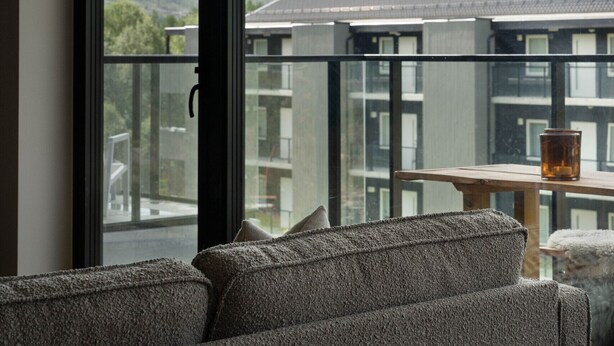 A modern living room with a large window, a sofa, and a table with a glass. - New (2023) apartment with very central location. (Hol)