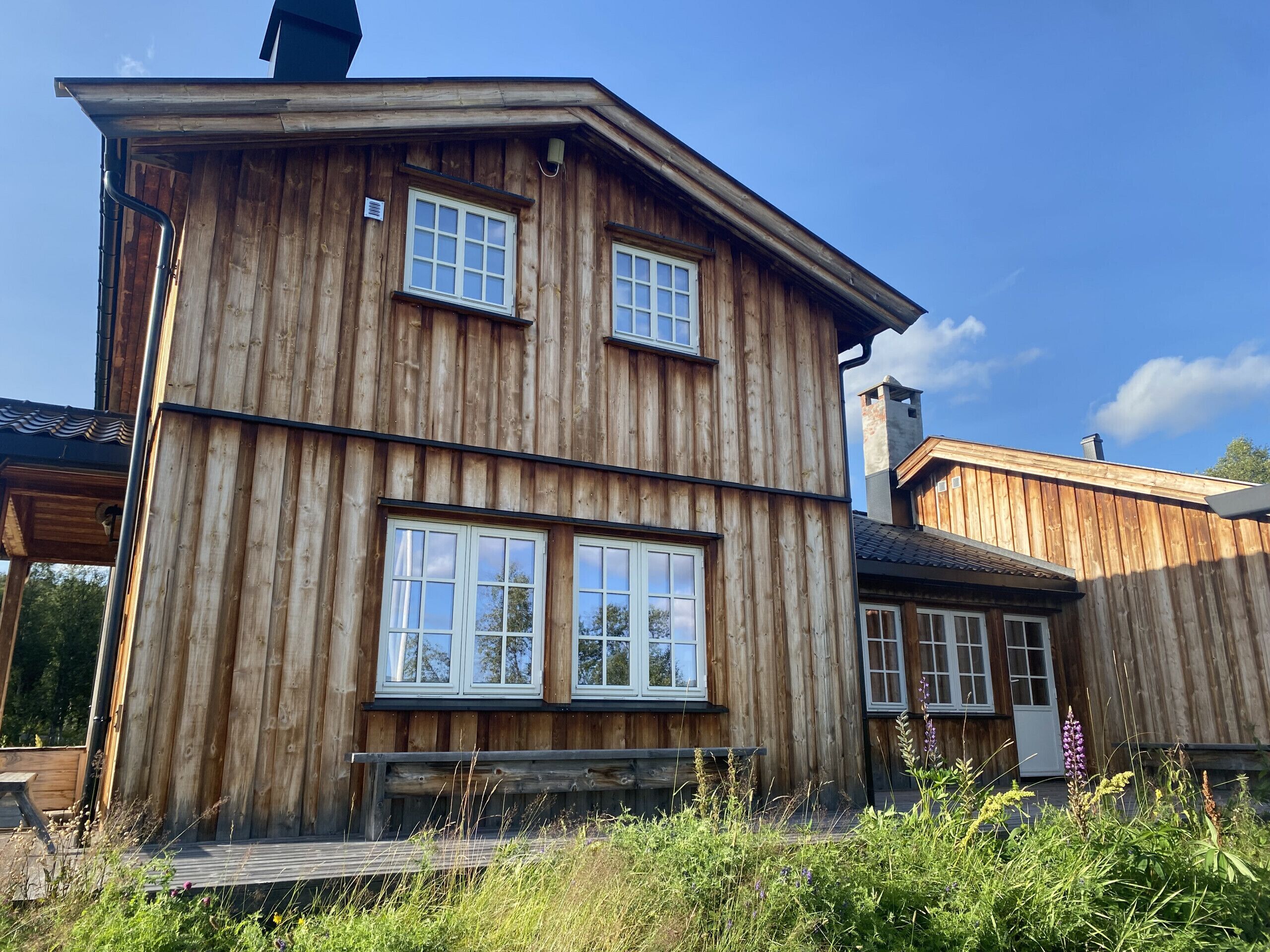 Une cabane en bois avec deux grandes fenêtres, une cheminée et une terrasse.