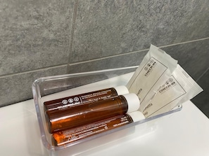 A bathroom with a clear plastic container holding a brown bottle and a white packet, likely containing toiletries. - GREEN WAVES HOME - A STONE'S THROW FROM LAKE ISEO (Villongo)
