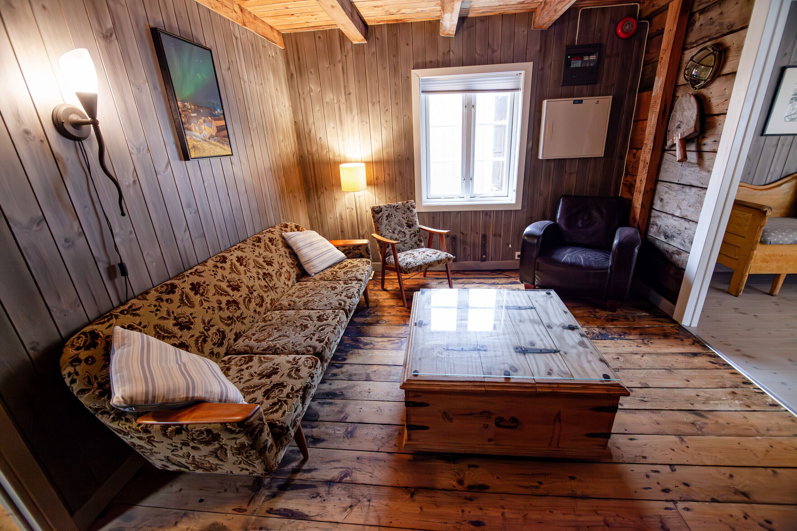 Une pièce chaleureuse avec un plancher en bois, un canapé, un fauteuil à motifs, un fauteuil en cuir, une table basse en bois et une fenêtre donnant sur un beau paysage.