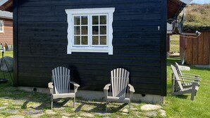 Une petite cabane en bois avec une fenêtre à cadre blanc et deux chaises Adirondack devant.