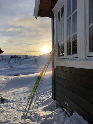 A snowy landscape with a house and skis leaning against the house.