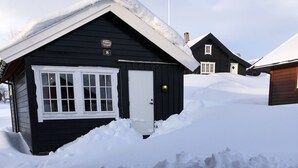 Une cabane en bois recouverte de neige, avec une porte et des fenêtres blanches, entourée de hautes congères.