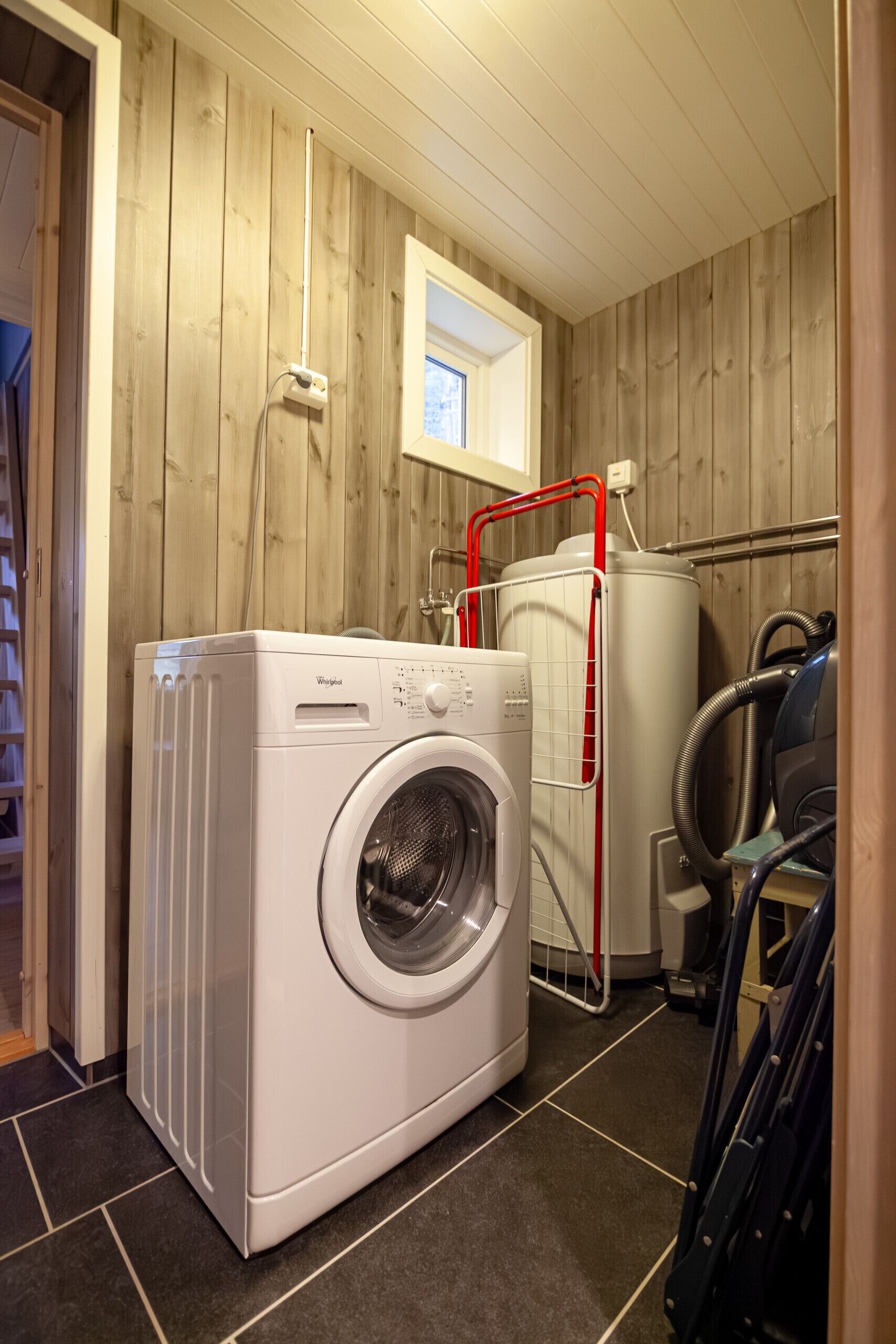 Een wasserette met een voorlader wasmachine en droger, een raam en een houten wand.
