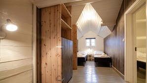 Un pasillo estrecho con paredes de madera, techo inclinado y dos camas con ropa blanca.