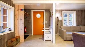 Una habitación con piso de madera, un sofá, una silla, una puerta con un ventanal circular y una pequeña mesa con un florero.