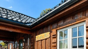 Una baita in legno con una terrazza, due sedie Adirondack e un cartello con la scritta 'Gästehaus Hoh'.