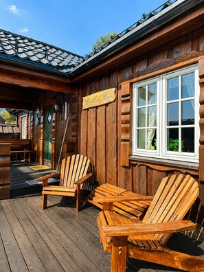Eine Holzhütte mit einer Veranda, zwei Adirondack-Stühlen und einem Schild mit der Aufschrift 'Gästehaus Hoh'.