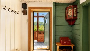 Un interno in legno con una porta che dà su un balcone, un attaccapanni, una scatola rossa con la scritta 'HAGEN' e un porta scarpe in legno.