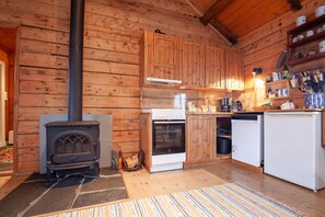 A wooden cabin interior with a wood stove, oven, dishwasher, and wooden cabinets. - Aronbua - Valen Cabins (Moskenes)