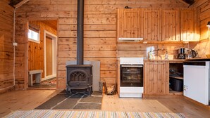 L’intérieur d’une cabane en bois, avec un poêle à bois, un four et un petit banc.