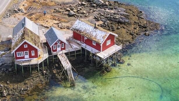 Une propriété située sur la côte, avec trois bâtiments rouges, une jetée en bois et une eau turquoise cristalline.