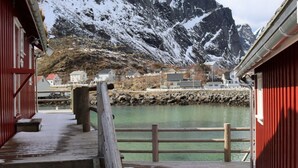 Une jetée en bois mène à un bâtiment rouge, d’où l’on peut admirer une montagne et une étendue d’eau calme.