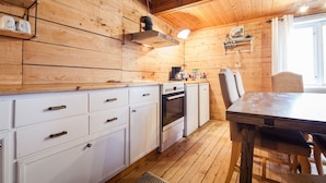 Interior em madeira com cozinha, incluindo armários, fogão e mesa de jantar.