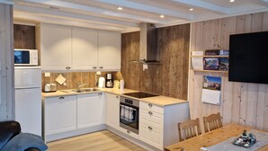 Une cuisine compacte avec des meubles blancs, un four à micro-ondes, une cuisinière et un évier. On y trouve une table à manger avec des chaises et une petite plante décorative.