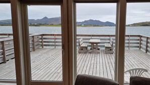 Une terrasse en bois avec une table et des bancs, offrant une vue sur un plan d’eau et des montagnes.