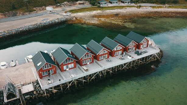 Une rangée de maisons en bois rouges, avec une jetée qui s’avance dans l’eau.