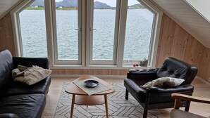Une pièce avec vue sur un lac, un canapé en cuir noir, une table basse en bois et un fauteuil en cuir noir.