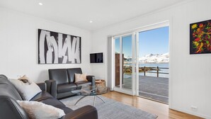 A modern living room with a sofa, coffee table, and artwork, leading to a sliding glass door with a snowy mountain view.