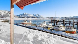 A marina with boats docked, snow-covered ground, and mountains in the background.
