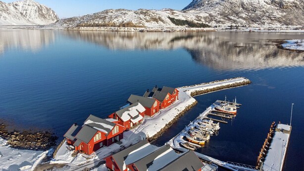 A waterfront property with a dock, a row of red buildings, and a snowy landscape.