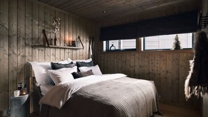 Una camera accogliente con parete in listelli di legno, un letto con biancheria da letto bianca e decorata, un comodino con una lampada e una finestra vista albero.
