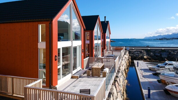 A row of wooden cabins with large windows, a stone wall, and a view of the sea.