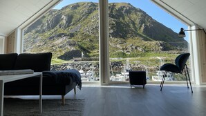 A room with a large window, a black sofa, a small table, and a chair.