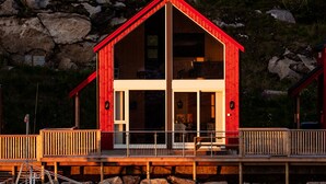 A red wooden cabin with a balcony, large windows, and a stone foundation.